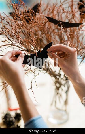 Human hands with black paper bat decorating dry branches for halloween Stock Photo