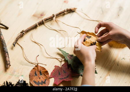 Hands of woman hanging dry leaves with drawn faces on stick over wooden table Stock Photo