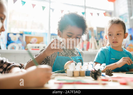 Serious schoolboy and his classmate painting Christmas decorations by desk Stock Photo
