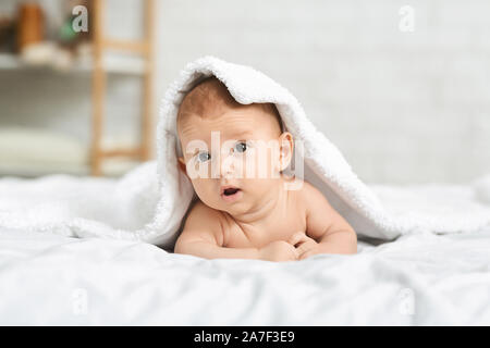 Cute newborn boy peeking out under soft white blanket Stock Photo