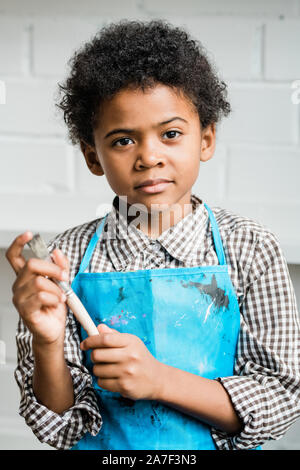 Creative and adorable schoolboy with paintbrush while standing in isolation Stock Photo