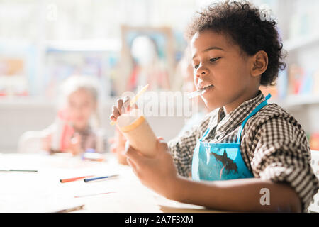 Contemporary schoolboy with crayon rolling piece of paper while making toy Stock Photo