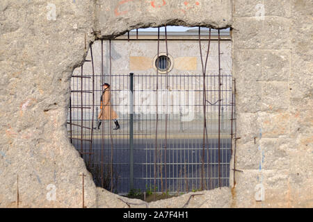 Berlin, Berlin, Germany. 1st Nov, 2019. A pedestrian can be seen through a hole of the remaining 200 meters of the Berlin Wall at NiederkirchnerstraÃŸe in Central Berlin. The Berlin Wall was massive border complex and became an international symbol of the division of Germany after the Second World War and also of the Cold War between East and West. November 9, 2019 will mark the 30th anniversary of the peaceful 'fall'' of the Wall on November 9, 1989. Credit: Jan Scheunert/ZUMA Wire/Alamy Live News Stock Photo