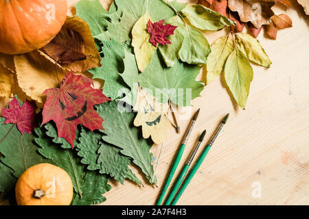Dry autumn foliage, gourds, halloween faces on leaves and paintbrushes Stock Photo