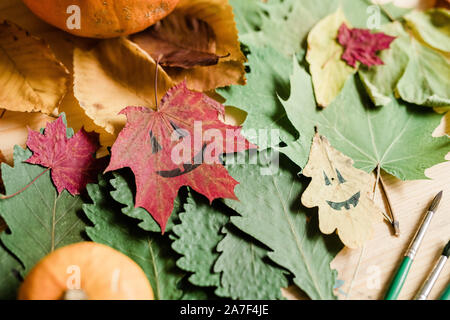 Background of dry autumn foliage, halloween faces on leaves and paintbrushes Stock Photo