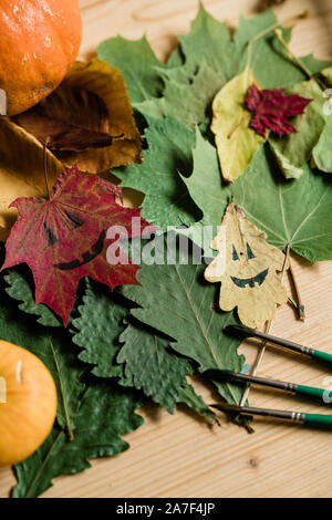 Overview of dry autumn foliage, drawn faces on leaves and three paintbrushes Stock Photo
