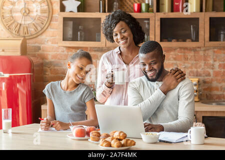 Lovely afro family having breakfast, watching photos on laptop Stock Photo