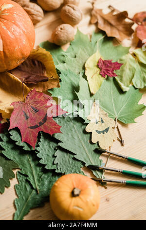 Dry foliage, pumpkins, walnuts, drawn faces on leaves and three paintbrushes Stock Photo