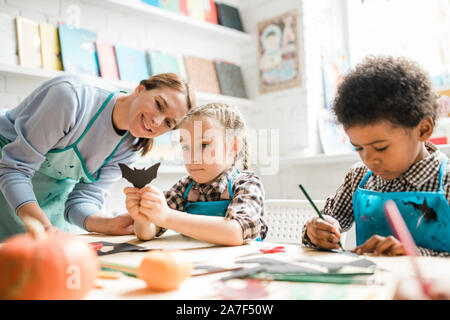 One of multicultural schoolkids showing handmade black paper bat to teacher Stock Photo