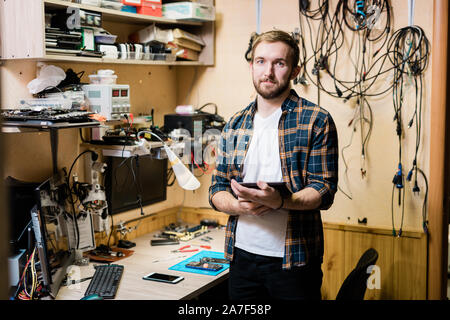 Young successful master in casualwear holding one of broken gadgets Stock Photo