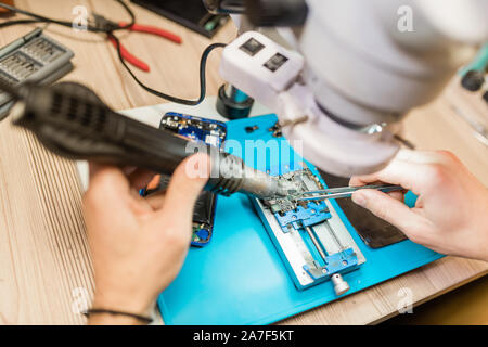 Electric handtool and tweezers in hands of repairman using microscope at work Stock Photo