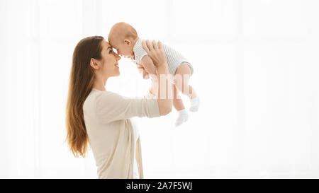Mother lifting her baby up against window at home Stock Photo