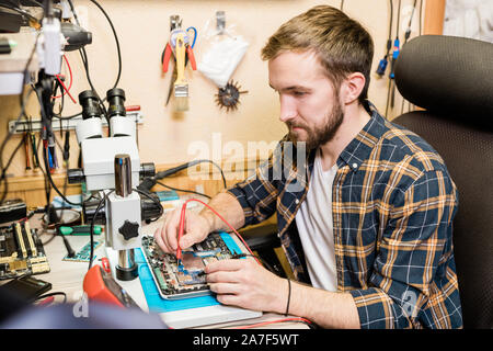 Young serious mechanic with two soldering-irons repairing demounted touchpad Stock Photo