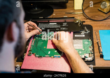 Tweezers in hands of repairman over demounted gadget working with tiny details Stock Photo