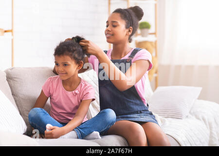 Caring african teenage girl brushing her little sister hair at home Stock Photo