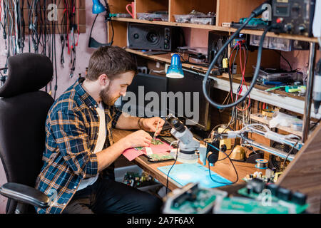 Young professional mechanic with small steel tweezers repairing demounted gadget Stock Photo
