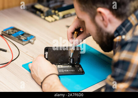 Professional gadget repair service master fixing tiny details with screwdriver Stock Photo