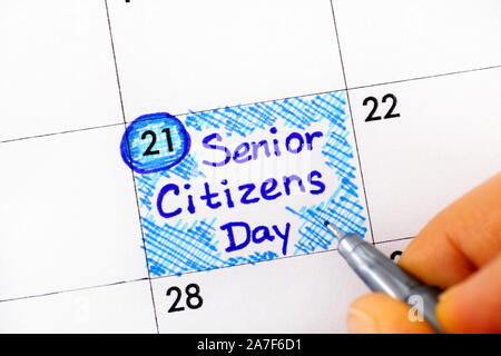 Woman fingers with pen writing reminder Senior Citizens Day in calendar. August 21st. Close-up. Stock Photo