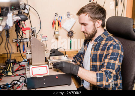 Bearded repairman in gloves sitting in front of equipment for gadget repair Stock Photo