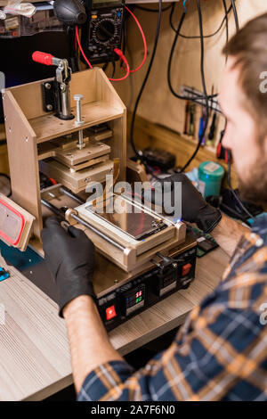 Professional repairman in protective gloves using equipment for gadget repair Stock Photo