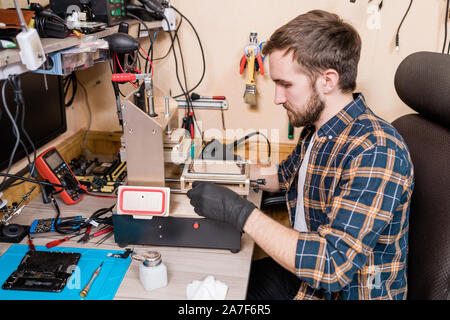Master of gadget repair service in protective gloves using special equipment Stock Photo