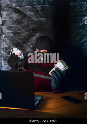 a bandit in a mask of a balaclava using a laptop does not fair profit on the Internet Stock Photo