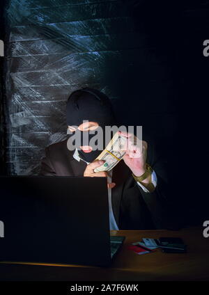 a bandit in a mask of a balaclava using a laptop does not fair profit on the Internet Stock Photo