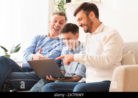 Boy Using Laptop Sitting Between Father And Grandfather On Couch Stock Photo