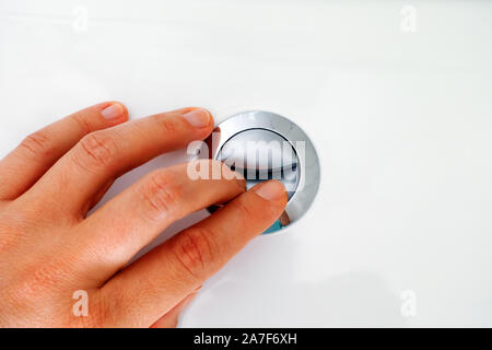 Womans hand pressing button for flushing. Close up. Stock Photo