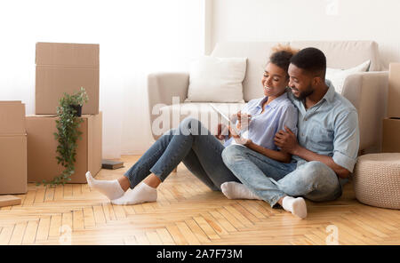 Spouses Using Tablet Sitting On Floor Among Unpacked Boxes Indoor Stock Photo