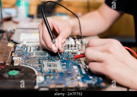 Hands of young master of gadget repair service using two small soldering-irons