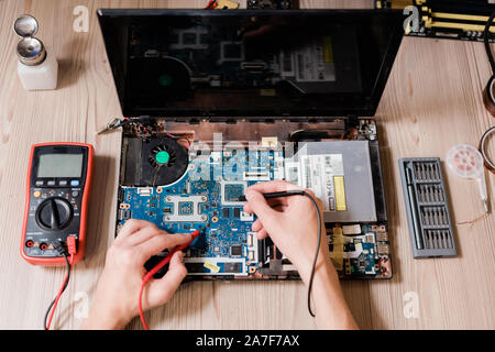 Hands of contemporary master using small soldering-irons to repair broken laptop Stock Photo
