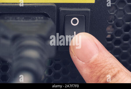 Finger switching on power supply system of PC. Close up. Stock Photo