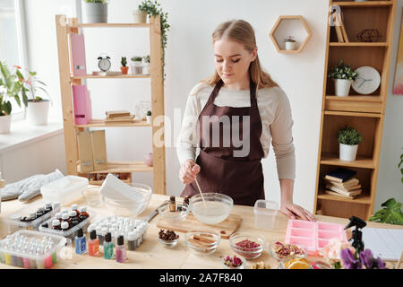 Craftswoman mixing liquid soap mass in bowl before pouring into silicone molds Stock Photo