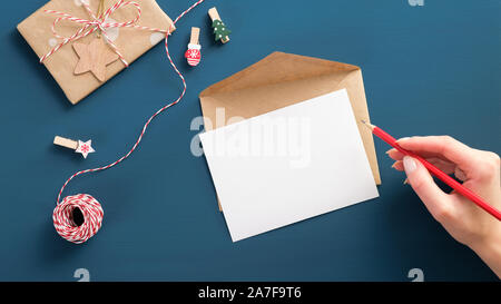Writing letter to Santa Claus concept. Flat lay white paper card, craft envelope, vintage gift box, wooden decorations on blue background. Christmas l Stock Photo