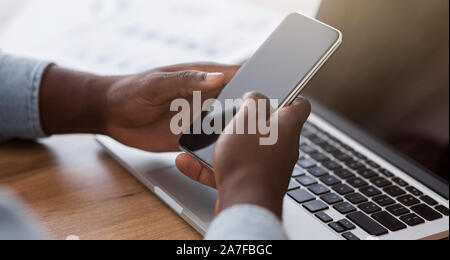 Black male hands using smartphone with blank screen and laptop Stock Photo