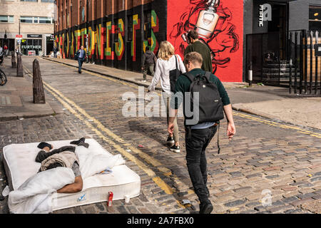 A rough sleeper is unaware of passers by in swanky Shoreditch, East London UK Stock Photo