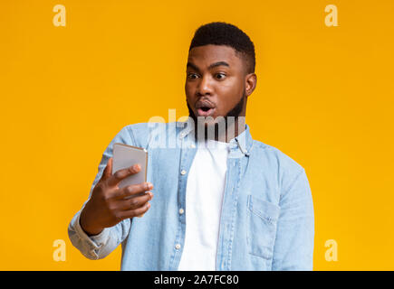 Surprised african man looking at smartphone screen with mouth opened Stock Photo