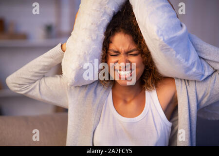 Angry student girl trying to sleep, covering ears with pillows Stock Photo