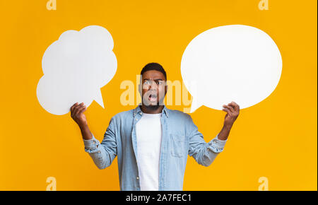Confused black guy holding two speech bubbles on yellow background Stock Photo