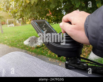 Close up of a disabled person hand driving electric wheelchair using joystick Stock Photo