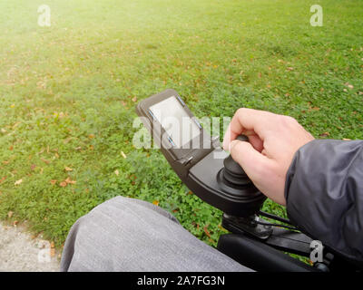Close up of a disabled person hand driving electric wheelchair using joystick Stock Photo
