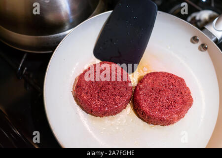 Closeup of two vegan meat sausage patties cooking on ceramic nonstick frying pan with oil grease spatula flipping Stock Photo