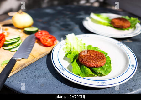 Cooked vegan meat sausage patty on plate with romaine lettuce leaf and cucumbers tomatoes sliced for burger Stock Photo