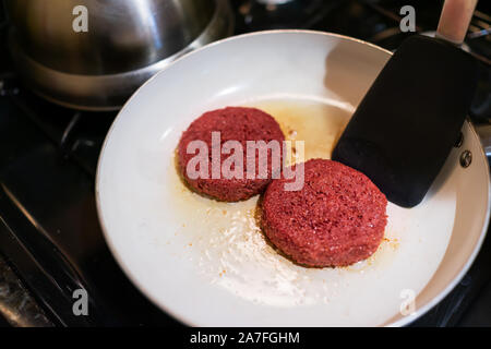 Closeup of two raw vegan meat sausage patties cooking on ceramic nonstick frying pan with oil grease spatula flipping Stock Photo