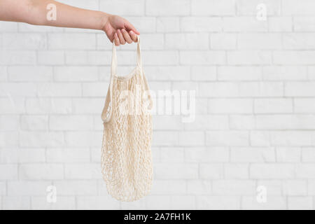 Woman holding empty eco net bag over white bricks wall Stock Photo
