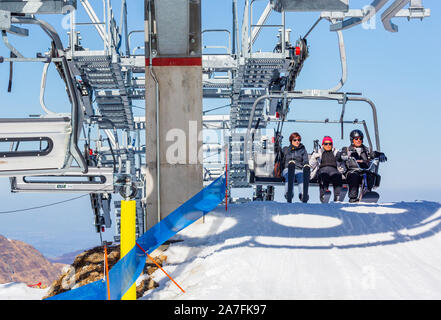 La Mongie, France - March 22, 2019:Front view of three skiers riding on chairlift arrival over snowy mountain slope while resting on resort on sunny w Stock Photo