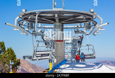 La Mongie, France - March 22, 2019:Front view of two skiers riding on chairlift arrival over snowy mountain slope while resting on resort on sunny win Stock Photo