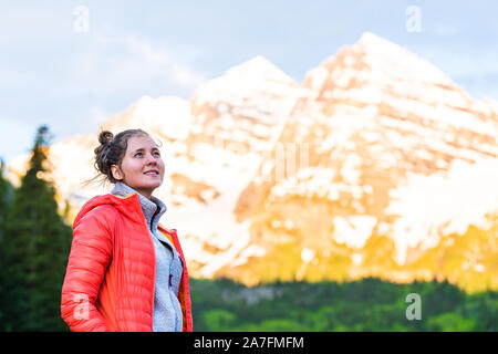Maroon Bells in Aspen, Colorado in June 2019 summer at sunrise with woman in jacket and ear muffs looking up at peak by lake Stock Photo