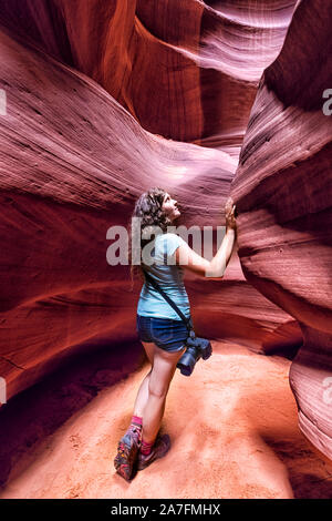 Young woman standing in desert landscape in Upper Antelope Canyon with sandstone rock and curve formations during summer touching wall Stock Photo